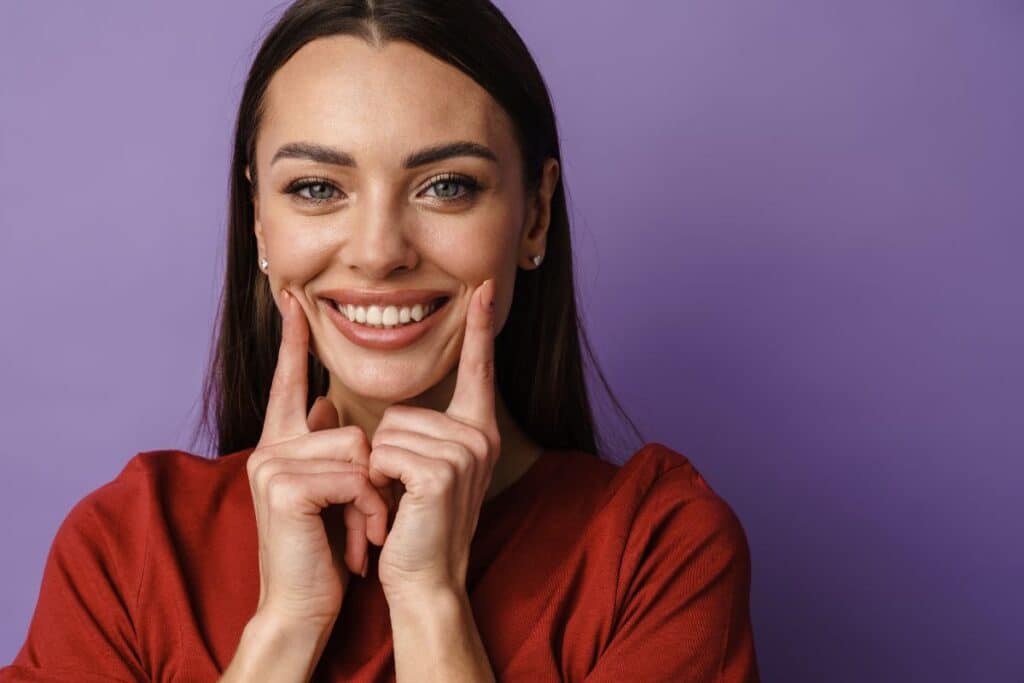 Woman smiling with hands to face, showcasing bright white teeth after professional whitening treatment.