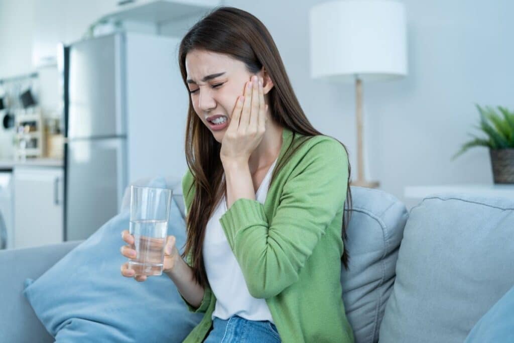Woman experiencing tooth pain while holding a glass of water.