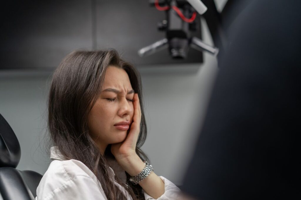 Woman experiencing dental pain holding her cheek in a dental office setting.